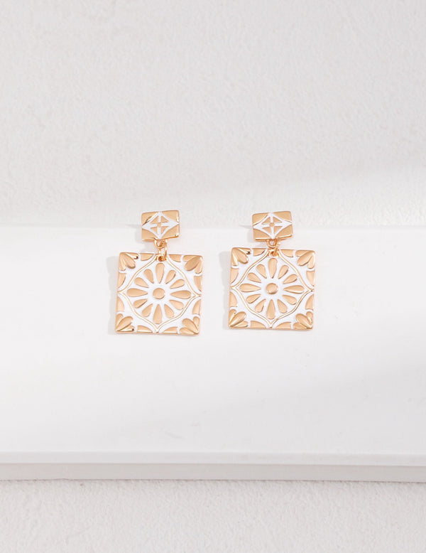 Exquisite drop studs with a vibrant white enamel inlay, set in a geometric square with a delicate floral design, crafted in gold.