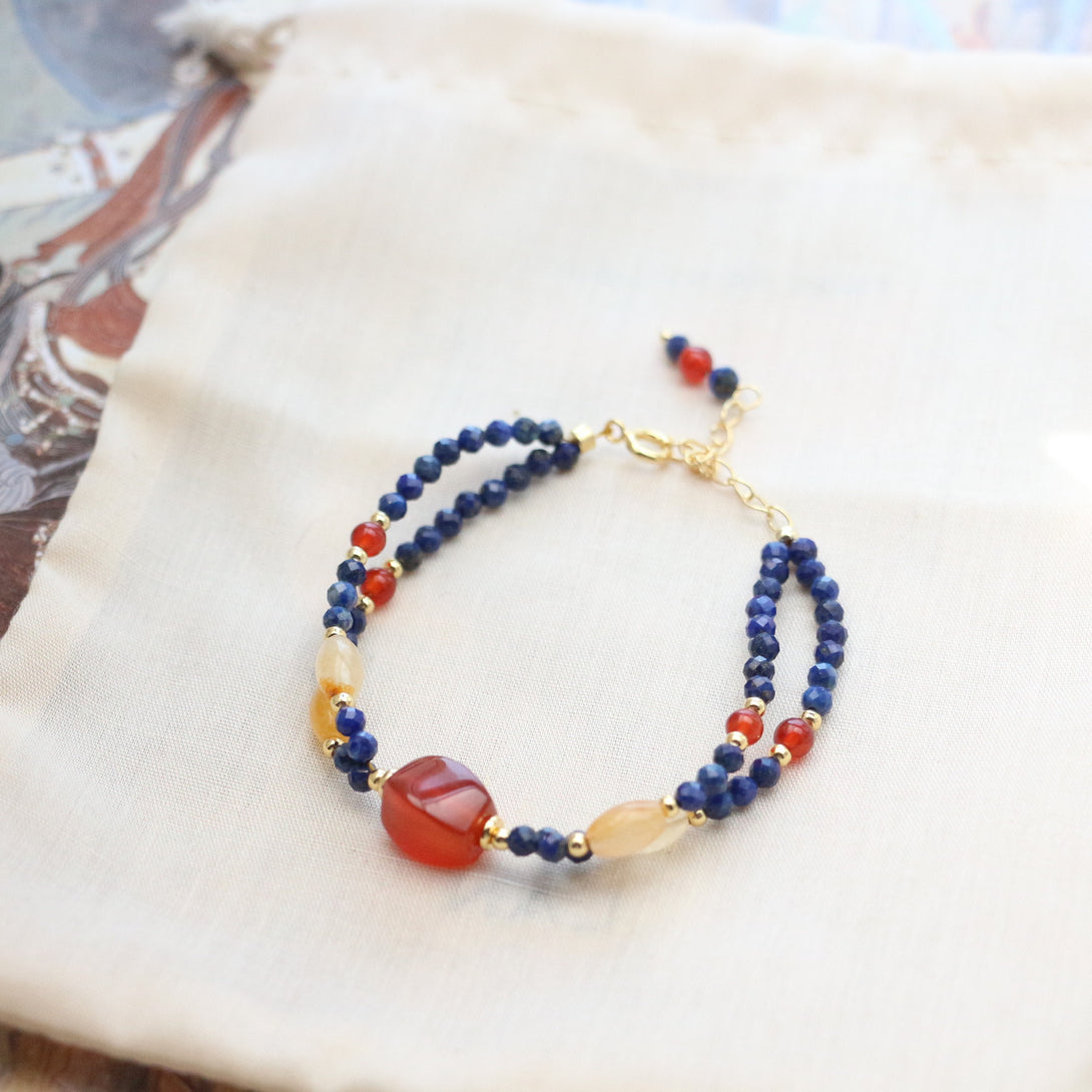 A double-strand beaded bracelet featuring natural citrine, lapis lazuli, and red agate gemstones, accented with 18K gold-plated elements. The bracelet showcases vibrant colors, with deep blue lapis lazuli beads, warm yellow citrine, and rich red agate stones, symbolizing energy, wisdom, and grounding strength. An adjustable gold-plated chain allows for a customizable fit (15-20cm).